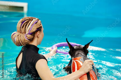 Foto Dog in life jacket swim in the swimming pool with coach