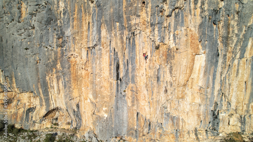 AERIAL: Gorgeous sunlit limestone wall with ascending young female rock climber AERIAL: Gorgeous sunlit limestone wall with ascending young female rock climber
