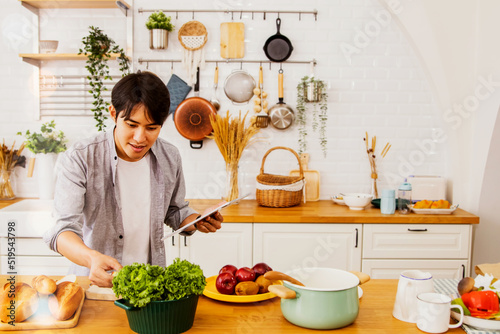Happiness in the kitchen : Handsome asian man uses his laptop to practice cooking in the kitchen by himself by taking online lessons from popular cooking shows  : Soft focus