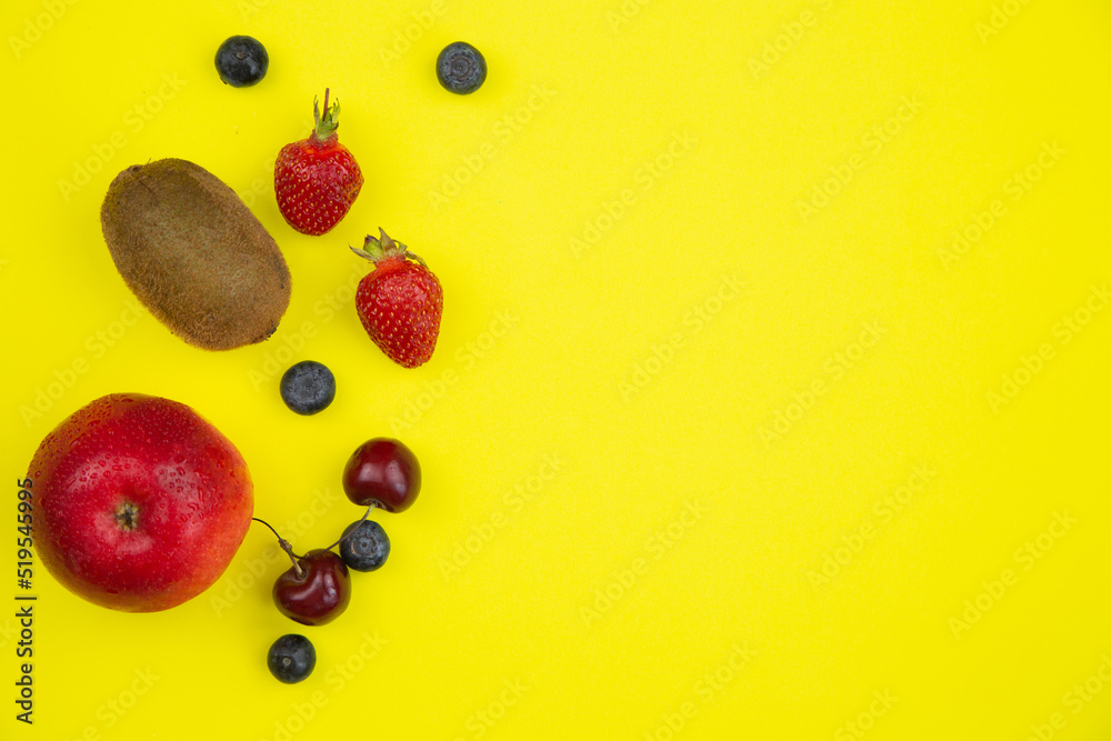 On a bright yellow background there are ripe fruits and berries on the left, on the right there is a place for text. High quality photo