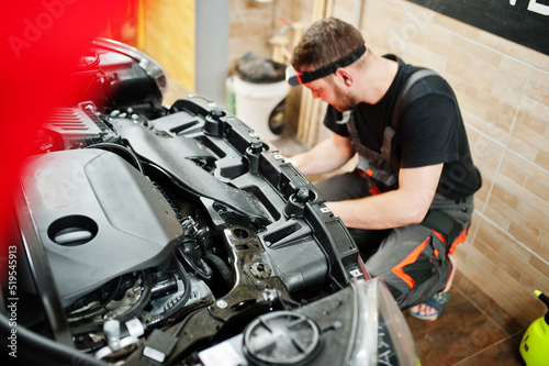 Car service worker put anti gravel film on a red car body at the detailing vehicle workshop. Car protection with special films.