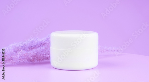 a white glass jar for moisturizing cream with a gold lid on purple or lilac background. Mockup for branding product packaging.