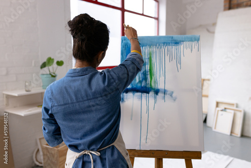 Image of back view of biracial female artist working on painting in studio photo