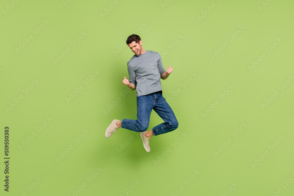 Full size photo of cheerful laughing man jumping raise fists in success triumph isolated on green color background Full size photo of cheerful laughing man jumping raise fists in success triumph isolated on green color background