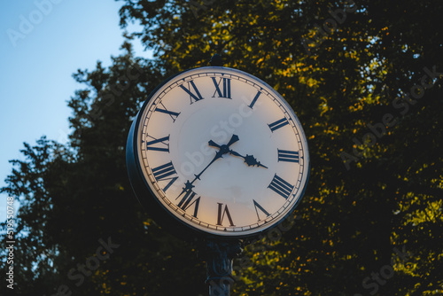 A vintage analog clock in the park in the early morning. Round street clock with Roman numerals
