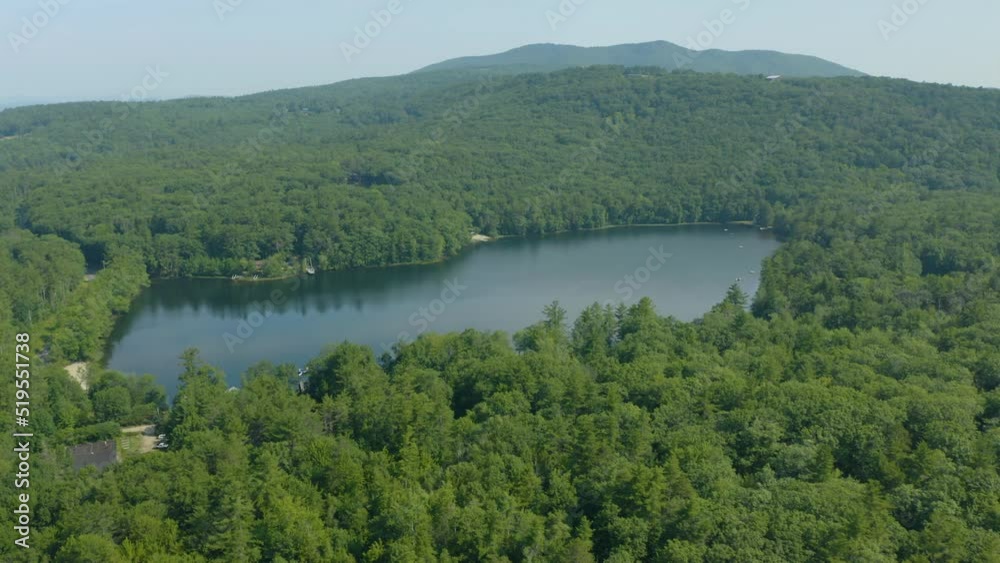 Aerial drone rotating shot over sunset lake surrounded by dense green coniferous forest over mountainous terrain at daytime. Calm water on warm beautiful summer day.