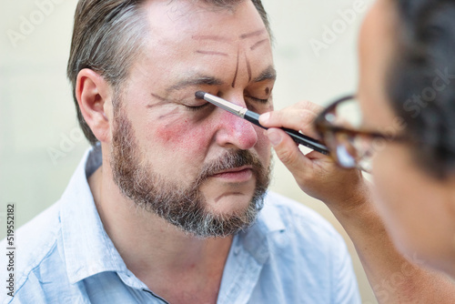 A theatre actor and a makeup artist applying rouge to his face and lines to make him look older