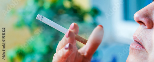 Middle age woman smoking cigarette.Close up of a female with a cigarette in her mouth.Blurred background.Side view.Banner advertisement.