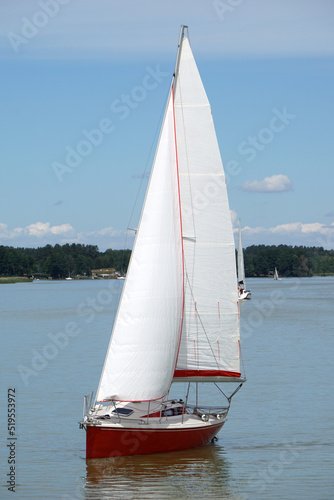 Fototapeta Naklejka Na Ścianę i Meble -  Red sailboat swimming on a lake, trees on shore