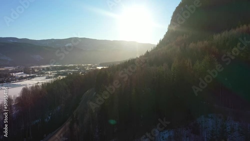 Spectacular winter sunrise above dark green forest in Nesbyen Hallingdal Norway - Backward moving aerial close to mountain while looking towards bright sun photo