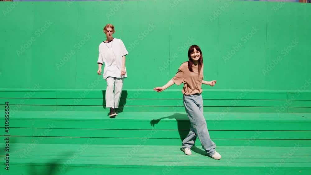 Young couple dancing hip hop on green background wall. Modern dance choreography. Professional dancers man and woman duet showing dance movings. Musical video.