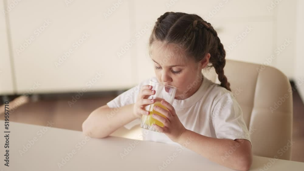girl child drinking juice indoors. happy family a healthy eating kid dream concept. daughter girl drinking yellow juice from a glass cup in the kitchen. child drinking fruit juice girl child drinking juice indoors. happy family a healthy eating kid dream concept. daughter girl drinking yellow juice from a glass cup in the kitchen. child drinking fruit juice