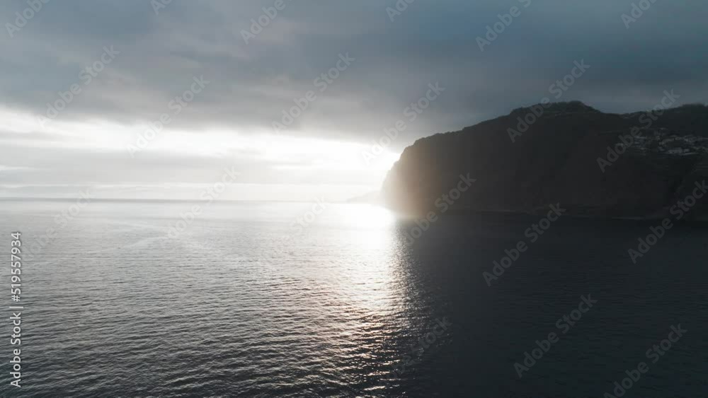 Cloudy Sunset Sky Over Funchal Bay In Madeira, Portugal. Massive Rocky Island In Silhouette Against Sunlight. wide drone shot Cloudy Sunset Sky Over Funchal Bay In Madeira, Portugal. Massive Rocky Island In Silhouette Against Sunlight. wide drone shot