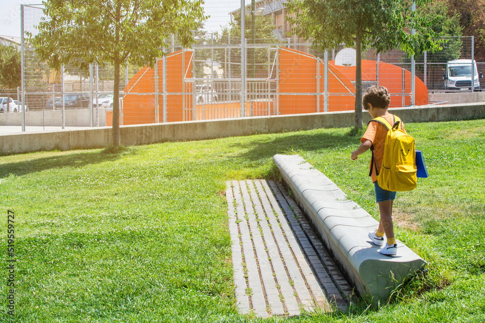 Rear view of a 7s boy with a backpack walking towards a school. A ...