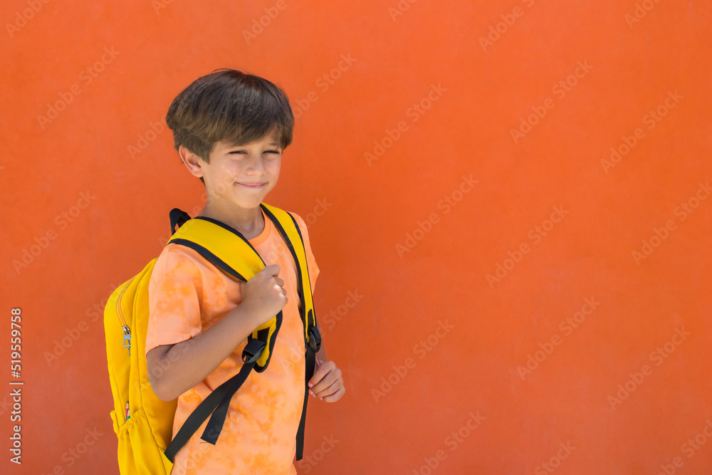 7-year-old schoolboy with a cheerful gesture with a yellow backpack, on an orange background. Image with copy space. Back to school. 7-year-old schoolboy with a cheerful gesture with a yellow backpack, on an orange background. Image with copy space. Back to school.