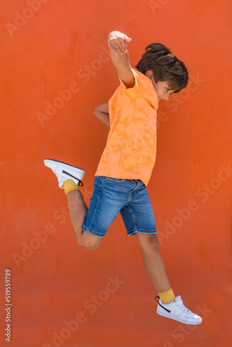 Elementary age 7 year old boy jumping on an orange background. Playful child with lots of vitality. Child jump