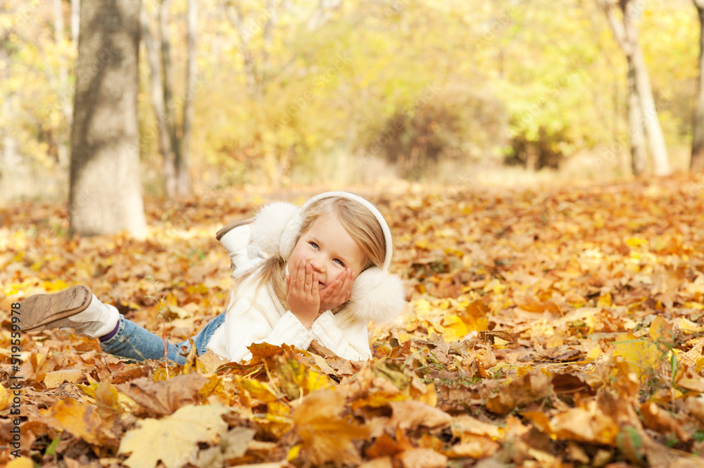 Happy girl portrait lying on autumn maple leaves and smiling in autumn park Happy girl portrait lying on autumn maple leaves and smiling in autumn park