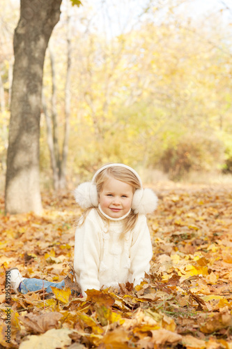 Happy blonde little girl portrait dressed in fur earmuffs  lying on autumn leaves