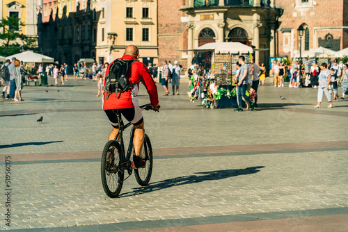 An adult cyclist in a red sports uniform with a backpack on his back rides a bike through the old town square in Krakow among the townspeople and tourists, sustainable transport, healthy lifestyle