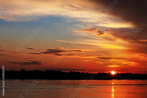 Sunset over the river. The sun sets below the horizon. Forest in the distance