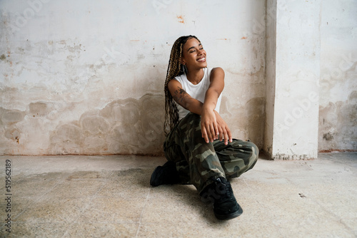 Beautiful multiracial girl sitting on the floor of a warehouse smiling dressed in a white t-shirt and military print pants.
