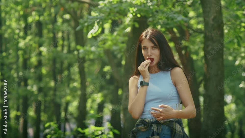 happy woman enjoying eating ripe strawberries while standing in the forest during family vacation. happy woman enjoying eating ripe strawberries while standing in the forest during family vacation.