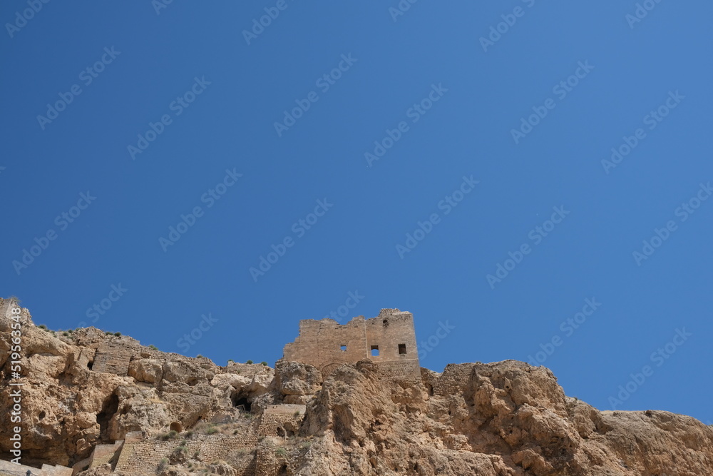 Old Mardin Castle from below with blue sky and rocks.