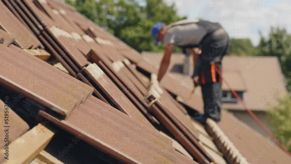 Roofer placing tiles in a house roof. Side view of construction work Roofer placing tiles in a house roof. Side view of construction work