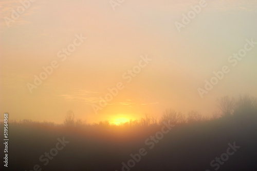 Beautiful sunrise over rural landscape with cold misty trees and orange skies