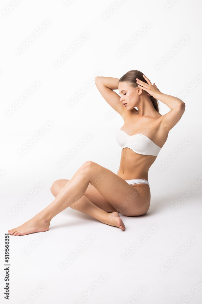 Studio shot of fit woman wearing seamless underwear in seating on the floor isolated on white. Slim attractive female with flat belly in white lingerie.
