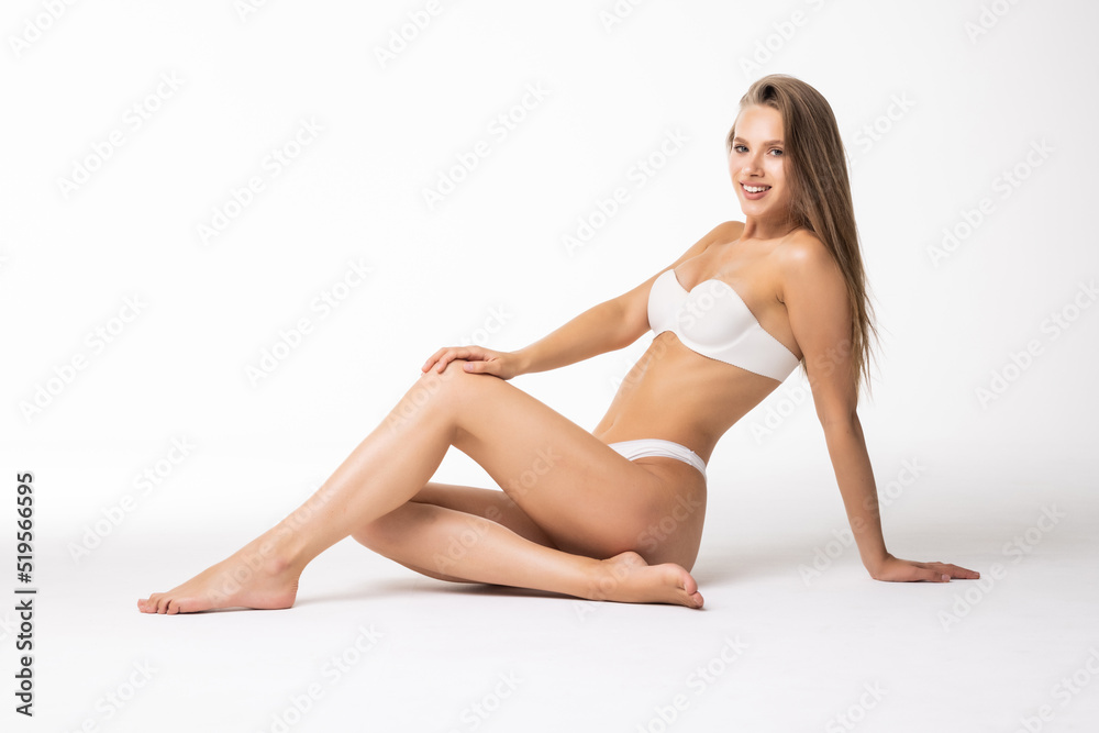 Young beautiful woman with perfect body in underwear sitting on floor posing on white background. Body care, female beauty, spa concept Young beautiful woman with perfect body in underwear sitting on floor posing on white background. Body care, female beauty, spa concept