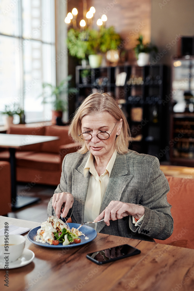 Mature businesswoman cutting vegetables on the plate, she eating salad during lunch at cafe