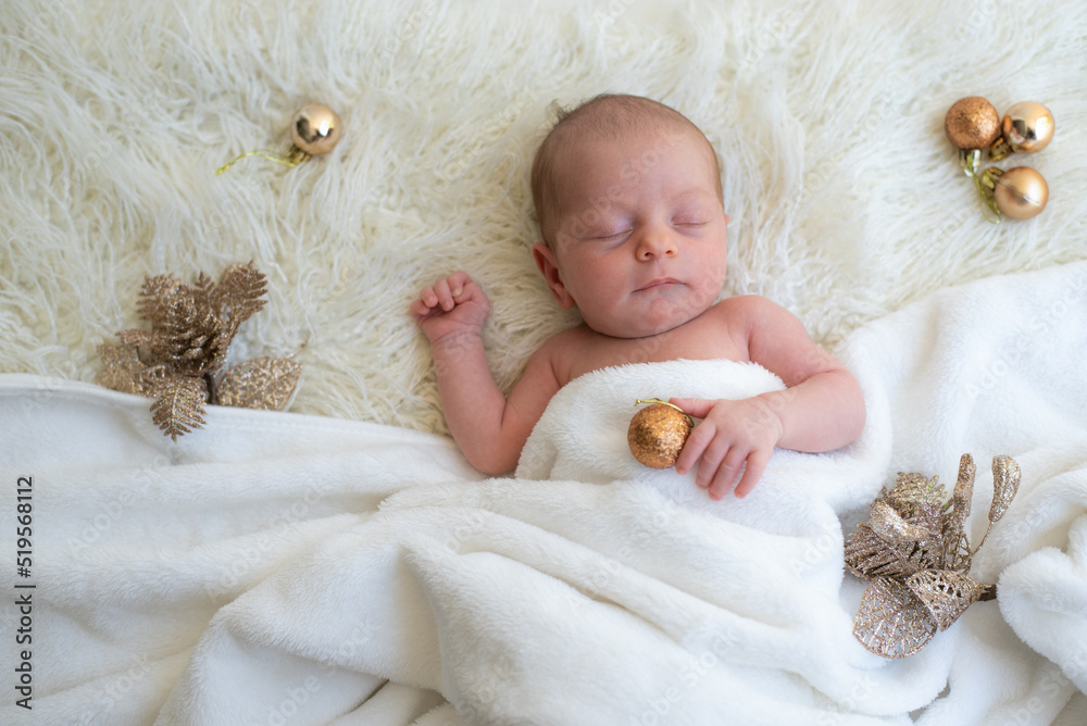 Baby holds golden ball in hand and soundly sleeps on white blanket decorate by golden balls and branches Christmas tree. Newborn is happiness for family. Top view. New year Baby holds golden ball in hand and soundly sleeps on white blanket decorate by golden balls and branches Christmas tree. Newborn is happiness for family. Top view. New year