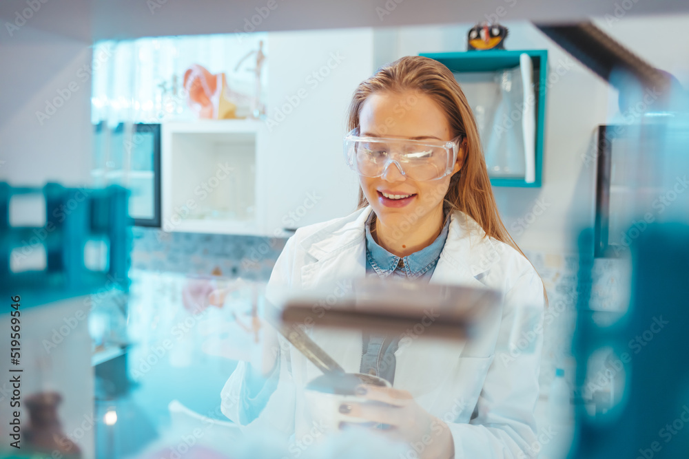 Close-up portrait of young scientist smiling. Confident female researcher is wearing protective eyewear. She is in science laboratory. State of the art science equipment. Close-up portrait of young scientist smiling. Confident female researcher is wearing protective eyewear. She is in science laboratory. State of the art science equipment.
