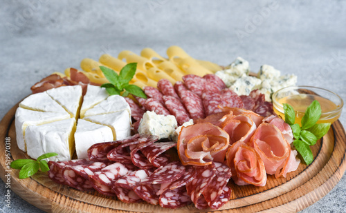 Wooden plate with delicacies. Brie cheese, blue cheese, salami, prosciutto on a wooden board.