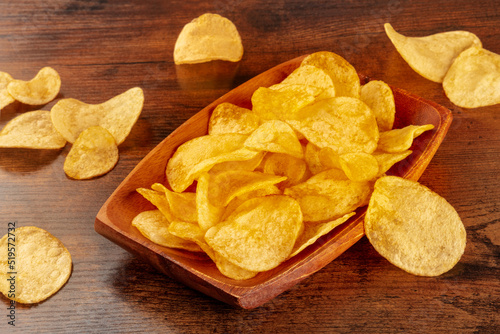 Potato chips or crisps in a bowl and scattered on a wooden table, a salty snack
