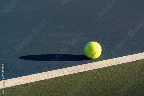 Yellow tennis ball at blue tennis court with white baseline and green out of bounds  © Thomas