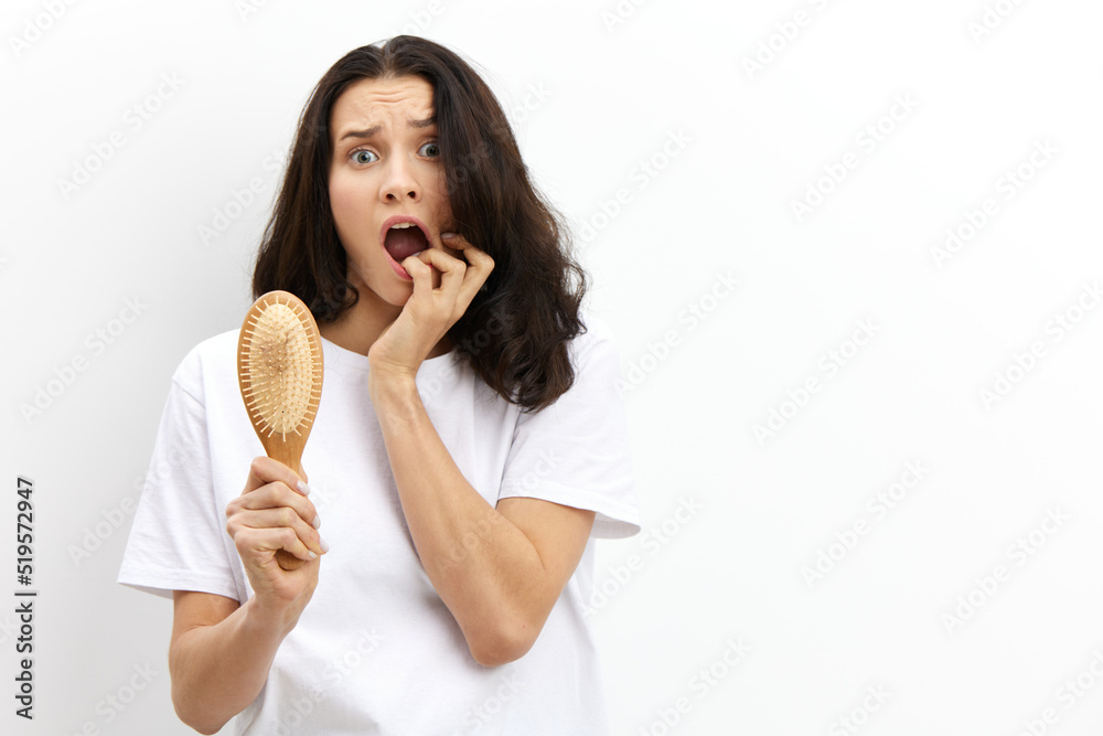 a sad, upset, puzzled woman with long black hair stands in a white T-shirt on a light background and holding her fingers to her mouth looks at camera a sad, upset, puzzled woman with long black hair stands in a white T-shirt on a light background and holding her fingers to her mouth looks at camera