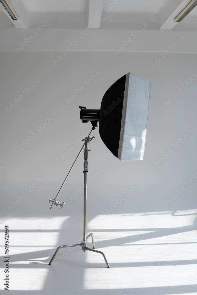 Professional photo flash light with a big softbox on a c-stand on a cyclorama in modern photo studio with a huge windows. Professional lighting equipment, flashes, c-stands.