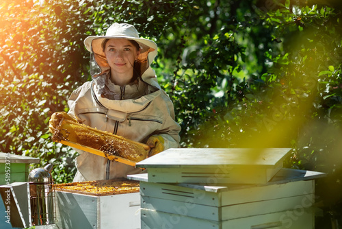 Young female beekeeper hold wooden frame with honeycomb. Collect honey. Beekeeper on apiary. Beekeeping concept.