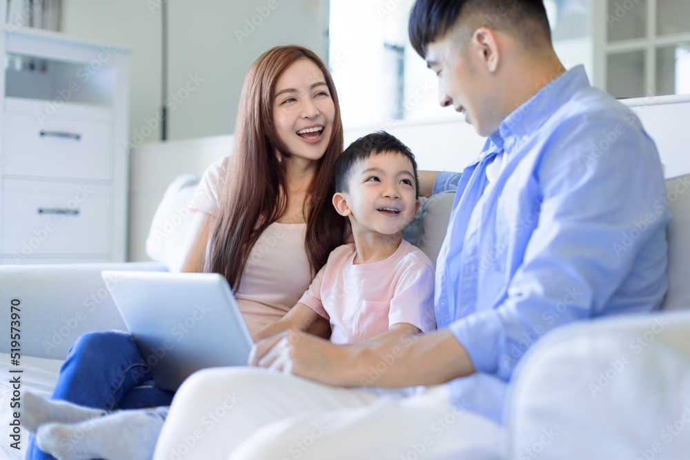 Fototapeta premium young happy cheerful family resting on sofa in living room using the laptop