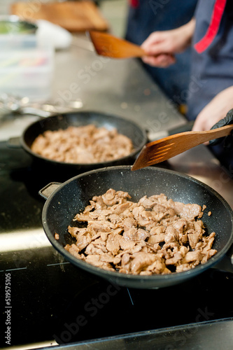 Cook fries meat in a pan with vegetables.