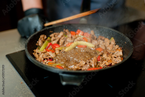 Cook fries meat in a pan with vegetables.