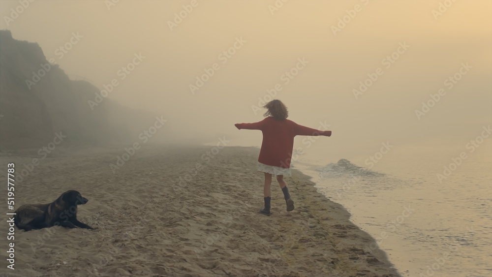 Happy girl running on ocean beach at sunrise. Excited girl raising hands