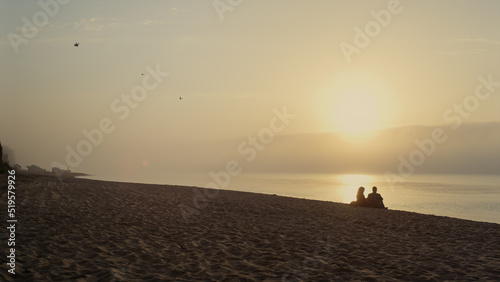 Young couple resting on beach at sunset. Wide shot lovers dating at ocean coast © stockbusters