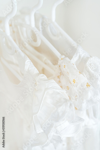 White summer children's dresses with flowers on hangers in wardrobe close up. Wooden Clothing Rack with children's outfits.