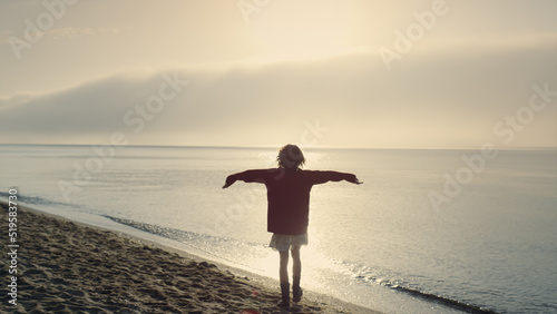 Happy girl spending vacation on beach at sunrise. Positive woman raising hands
