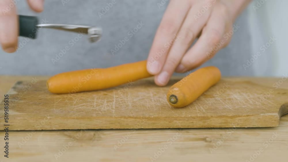 Two hands peel carrots using a vegetable peeler on a wooden cutting board Two hands peel carrots using a vegetable peeler on a wooden cutting board