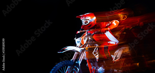 Fototapeta Naklejka Na Ścianę i Meble -  Portrait of young man, biker in full equipment riding motorbike isolated over black studio background with mixed lights. Flyer