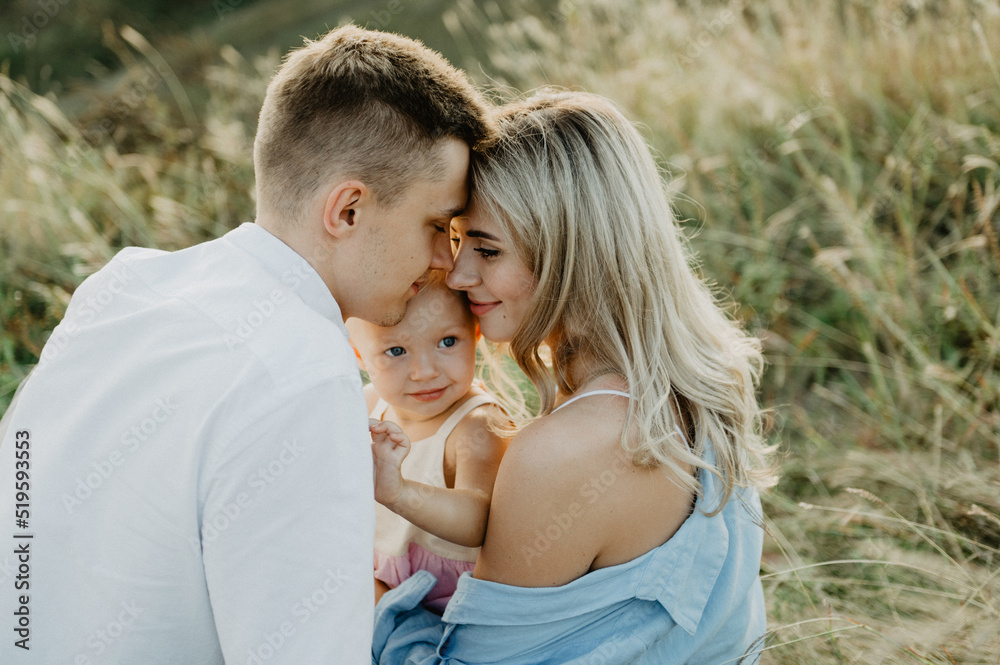 A young family with a little daughter are hugging and walking in the field at sunset. A young family with a little daughter are hugging and walking in the field at sunset.
